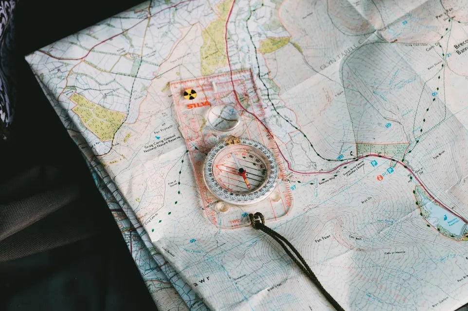 Baseplate compass resting on a folded topographic map with contour lines, paths and grid references