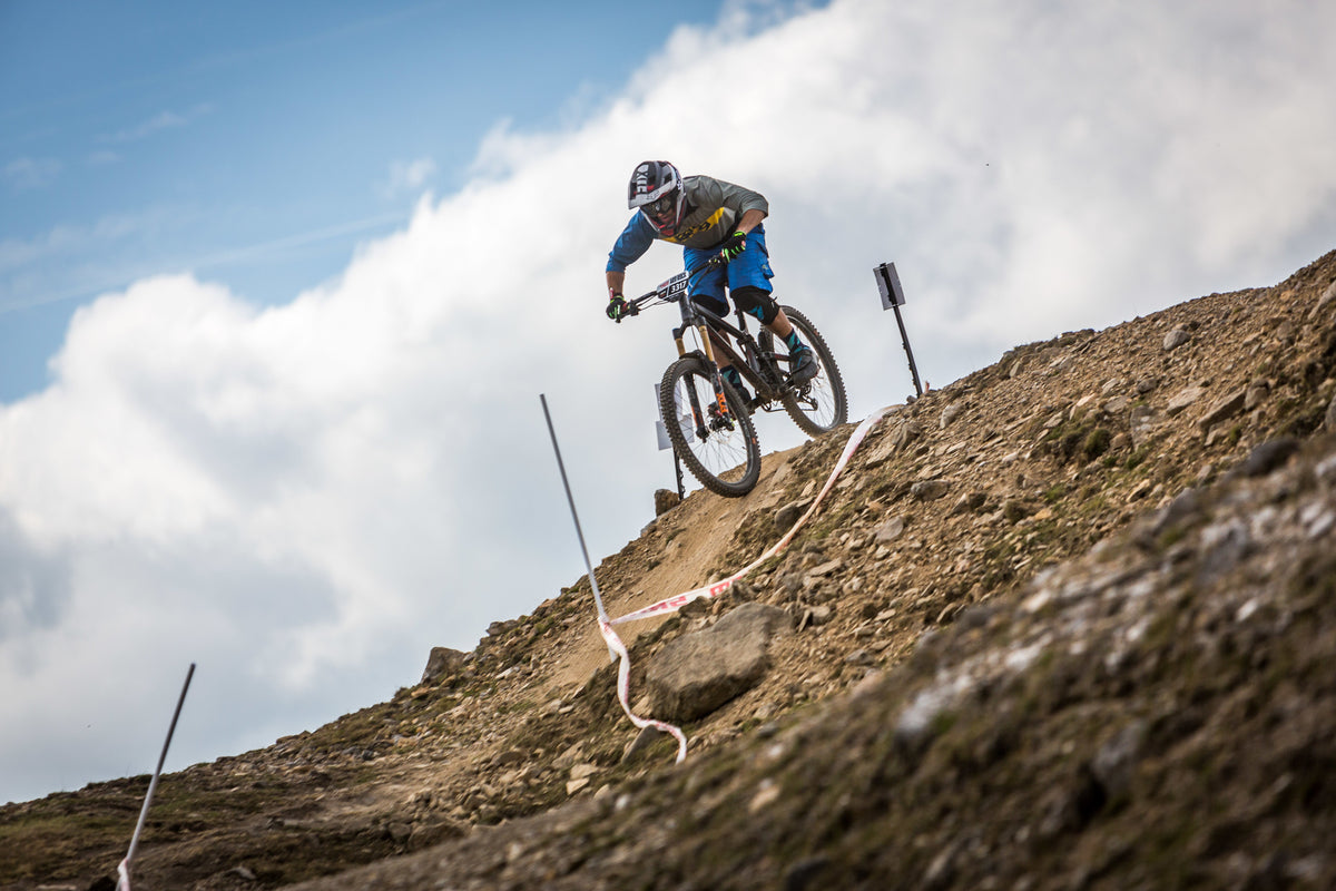 Downhill mountain biker with a race number descending a steep, rocky trail marked off with tape