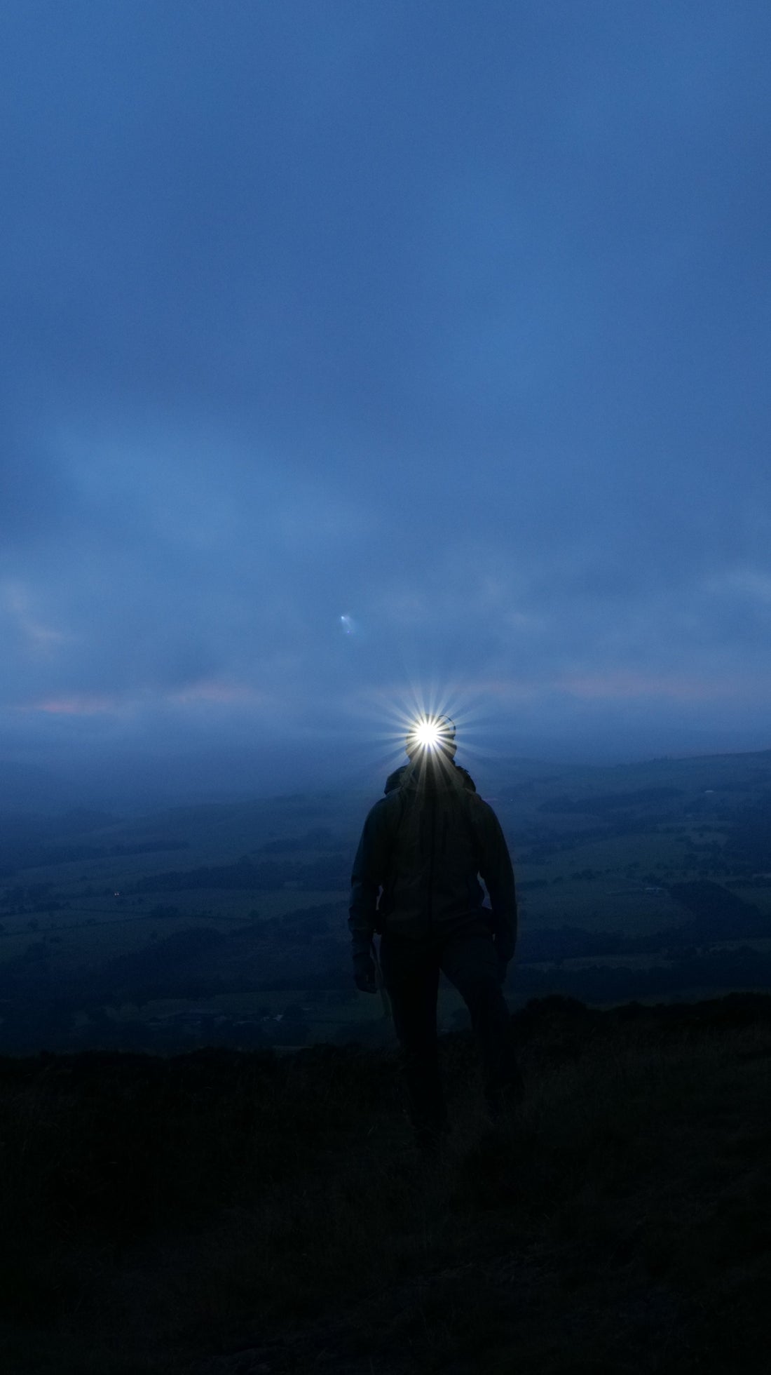 Hiker using a headtorch while walking on a UK hill after dark