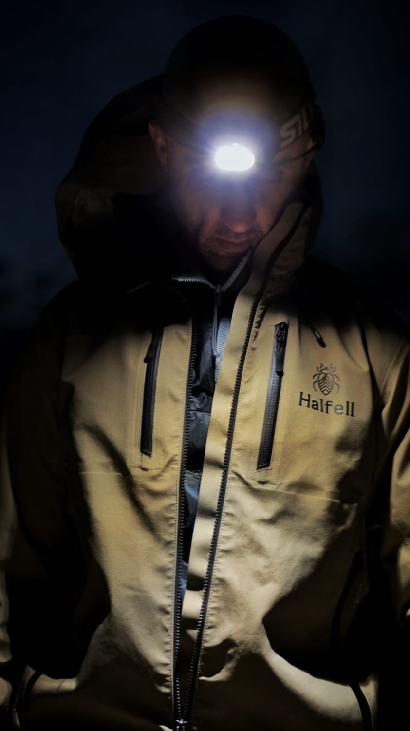 Man wearing a Halfell jacket at night with a headlamp lit, close on the embroidered chest logo