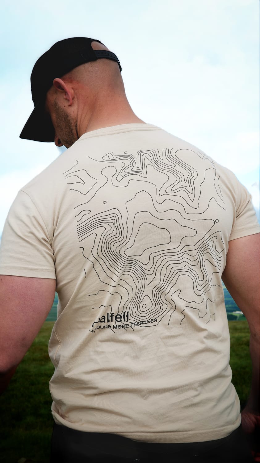 Man wearing the Halfell Origins T-Shirt in sand from behind, showing the topographic map print across the back
