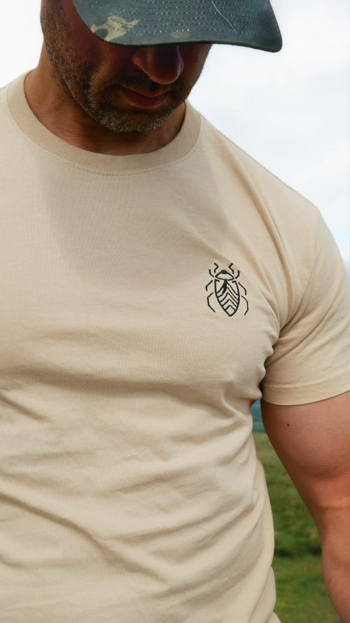 Man wearing the Halfell Origins T-Shirt in sand, close-up of the embroidered beetle logo on the chest